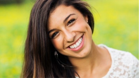 Young woman with long brown hair grinning outdoors