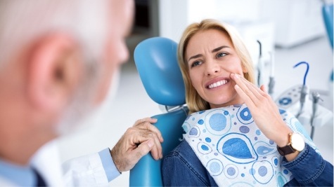 Woman holding her cheek in pain while sitting in dental chair