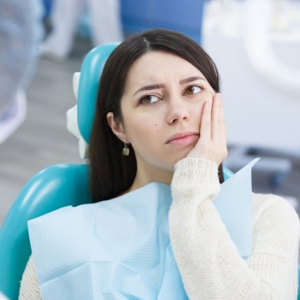 Dental patient in white sweater holding her cheek in pain