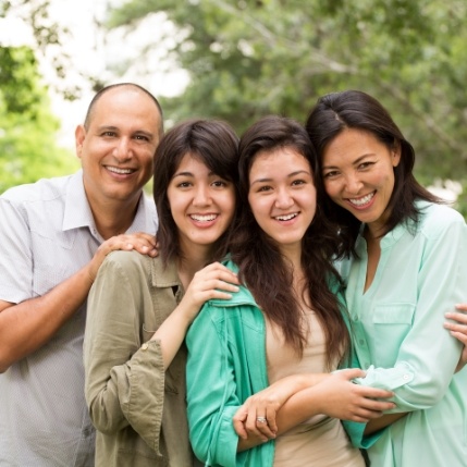 Family of four smiling outdoors after preventive dentistry visit
