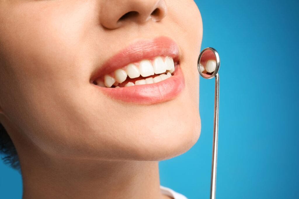 Nose-to-neck view of woman smiling with dental mirror reflecting teeth